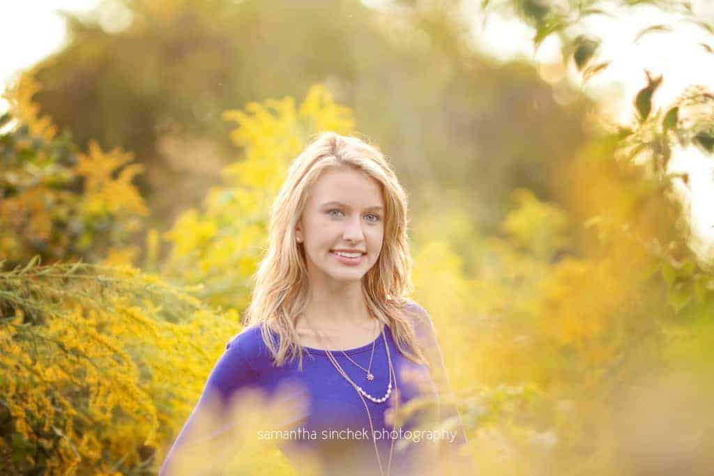 senior girl in surrounds herself with yellow flowers